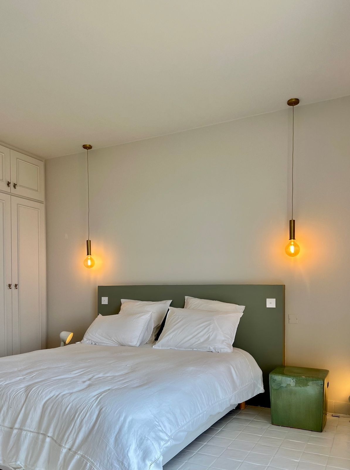 A bedroom with a bed, two bedside lamps, a green nightstand, and a white wardrobe.