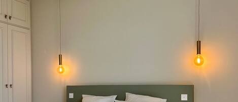 A bedroom with a bed, two bedside lamps, a green nightstand, and a white wardrobe.
