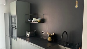 A modern kitchen with a built-in oven, a sink, and a countertop with a coffee maker and utensils. - Apartment facing the sea (Ajaccio)