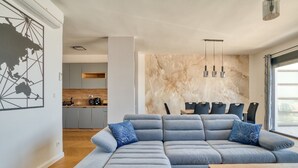 A modern living room with a sectional sofa, a wooden coffee table, and a dining area with chairs and a table. - Apartment Benita (Sveti Stefan)
