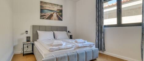 A bedroom with a bed, a nightstand, a painting, and a window with curtains.