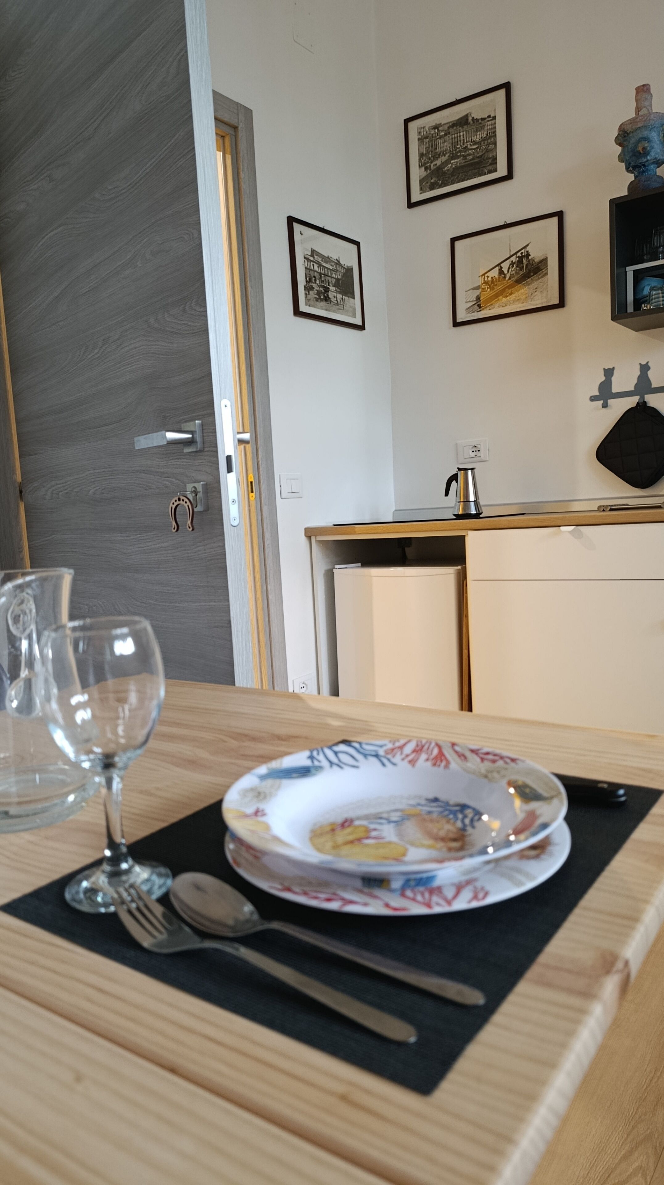 A dining area with a table set for two, featuring a plate with a floral pattern, a wine glass, and cutlery.