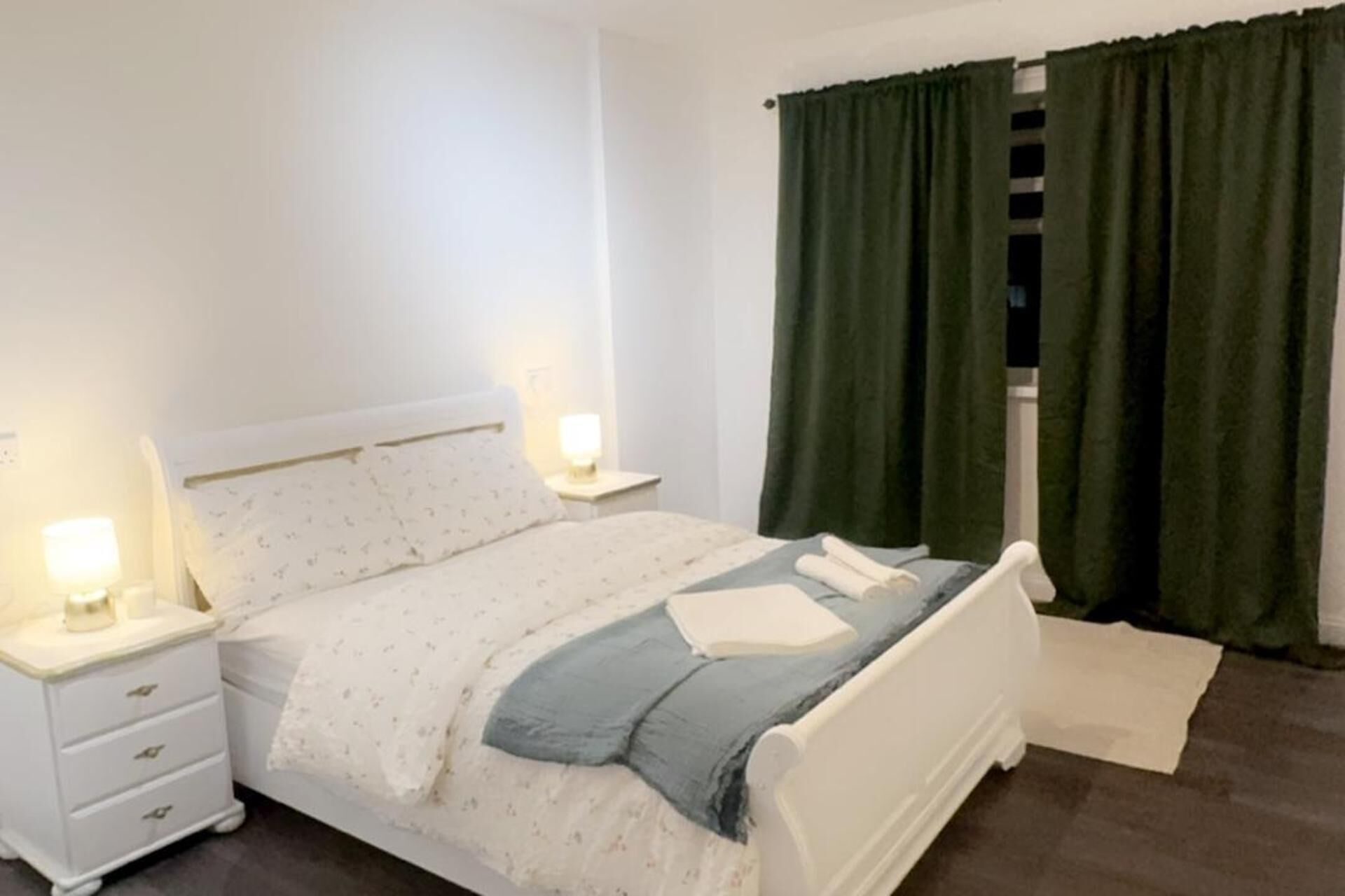 A bedroom with a bed, nightstands, a lamp, and green curtains.
