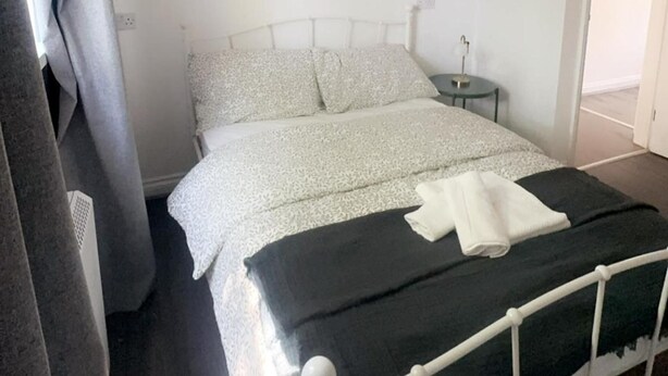 A bed with a white and grey patterned bedspread, a black blanket, and a white towel on the bed.