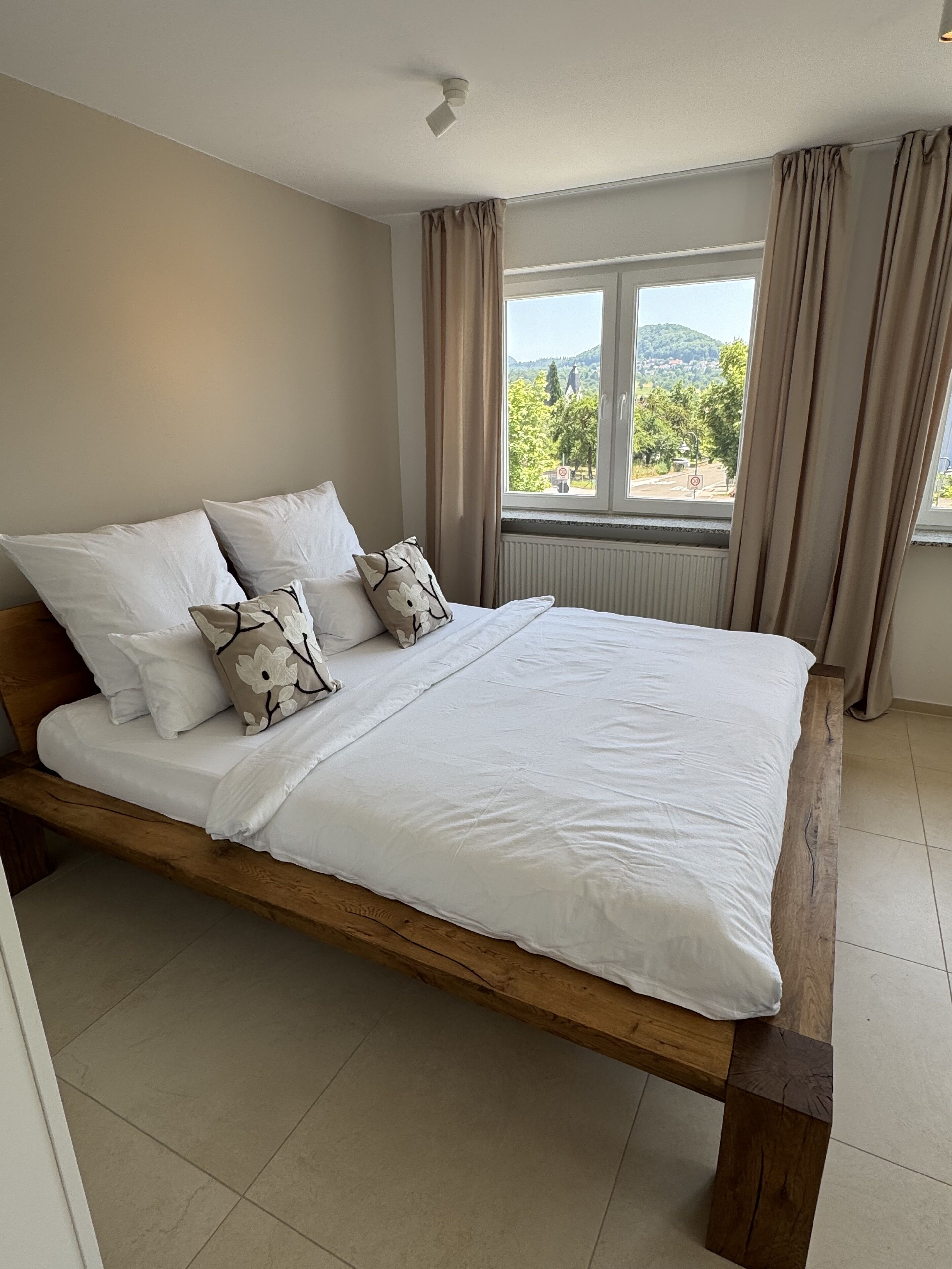 A bedroom with a wooden bed, white bedding, and a window with curtains.