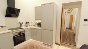 Uma cozinha moderna com uma lava-louças Bosch, micro-ondas e chaleira. Possui piso de madeira e uma porta que dá para outro cômodo.