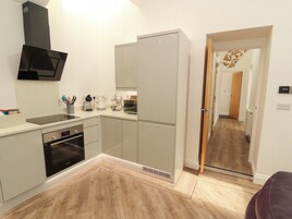 Una cocina moderna con lavavajillas Bosch, microondas y hervidor. El suelo es de madera y hay una puerta que conduce a otra habitación.