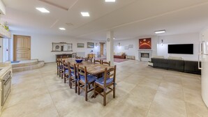 A spacious living area with a dining table, chairs, a sofa, a fireplace, and a TV.