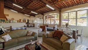 A spacious living area with leather sofas, a coffee table, and a dining table with chairs. A large window provides a view of the outdoors. - Ch Cara Tima Localiza o Piscina e Churrasqueira (Igarata)