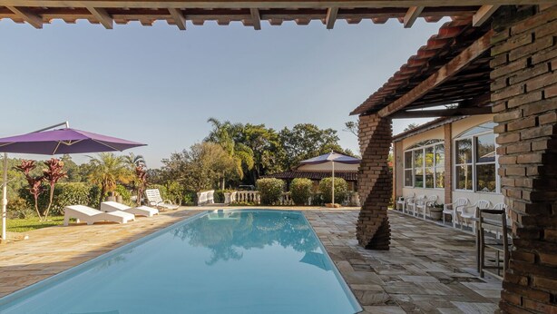 A swimming pool with lounge chairs and umbrellas, surrounded by a brick patio and greenery. - Ch Cara Tima Localiza o Piscina e Churrasqueira (Igarata)