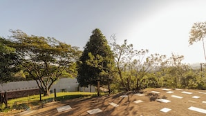 A paved area with rectangular markings, surrounded by trees and a building with a white facade. - Ch Cara Tima Localiza o Piscina e Churrasqueira (Igarata)