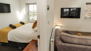 A hotel room with a bed, a sofa, a TV, and a window with blinds. - Lakes View Apartment 2 (Carnforth)