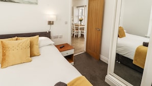 A hotel room with a bed, bedside table, lamp, and a mirror. - Lakes View Apartment 2 (Carnforth)