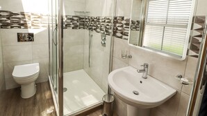 A modern bathroom with a glass-enclosed shower, a white toilet, and a sink with a mirror above it. - Lakes View Apartment 2 (Carnforth)