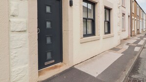 A row of terraced houses with a black door and windows, a narrow street, and a visible number '179' on the building. - Lakes View Apartment 2 (Carnforth)
