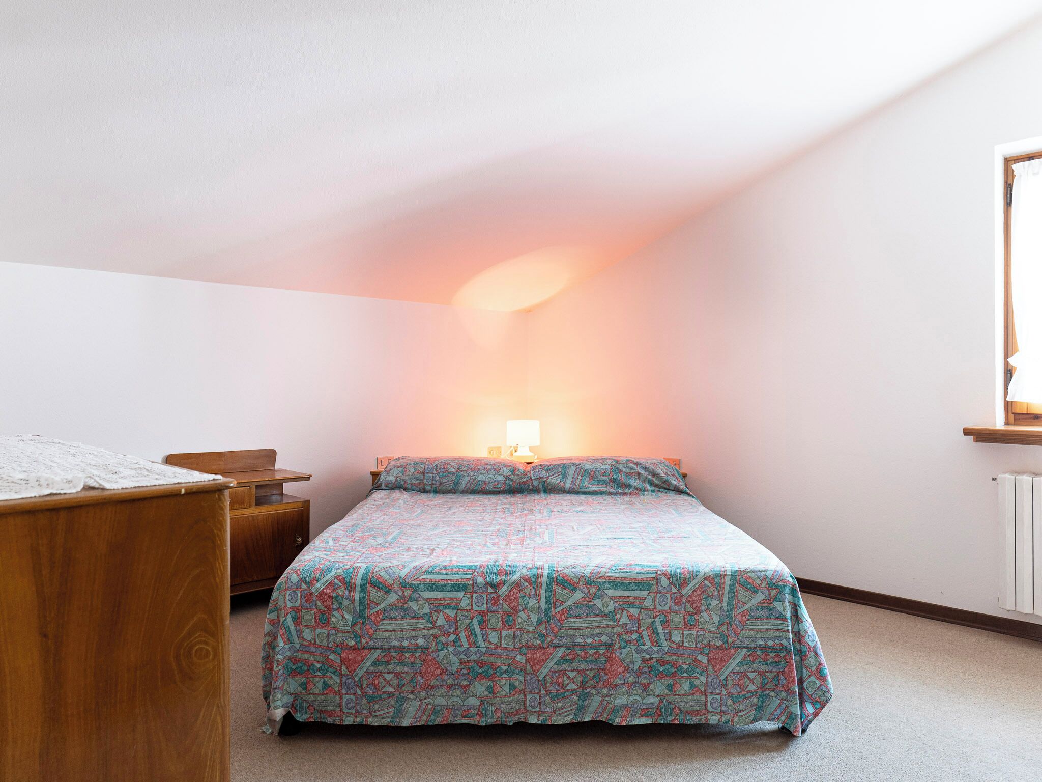 Een slaapkamer met een bed, een houten nachtkastje en een bureau.