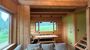 Interior acogedor de una cabaña con techo de madera, una mesa de comedor y un sofá con cojines estampados.