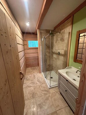Une salle de bain aux murs lambrissés, dotée d’une douche en verre, d’un lavabo et d’une fenêtre.