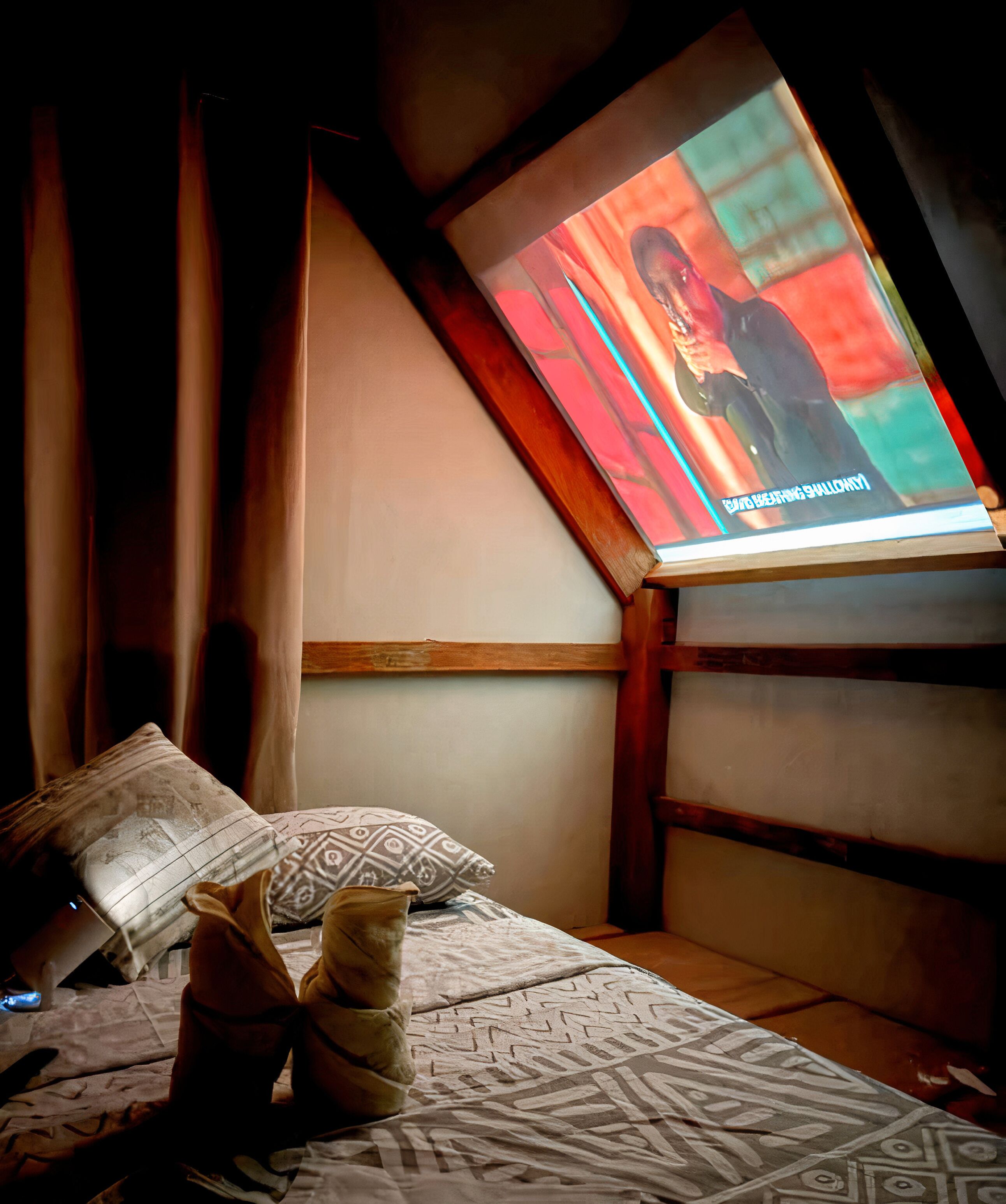 Una camera da letto con soffitto spiovente, un letto con biancheria a motivi decorativi e uno schermo televisivo che mostra un programma.