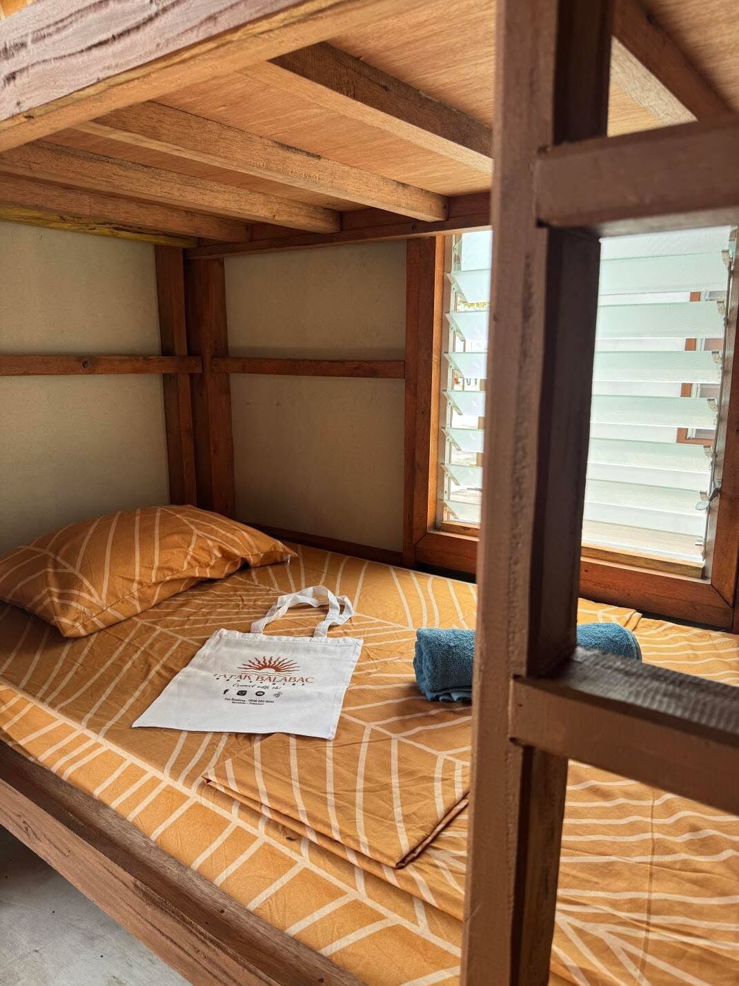 A bunk bed with a patterned bedspread, a pillow, a towel, and a tote bag on the bed.