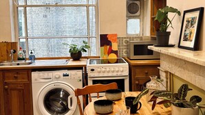 Una cocina compacta con lavadora, una mesa de comedor con sillas, microondas y una planta en maceta.
