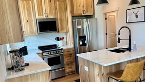 Una cocina moderna con armarios de madera, electrodomésticos de acero inoxidable, un salpicadero de mármol y una isla central con un taburete de bar.