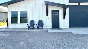 Una casa con garaje, dos sillas Adirondack y un camino de entrada de grava.
