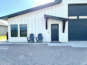 A house with a garage, two Adirondack chairs, and a gravel driveway.