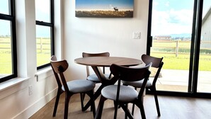Un área de comedor con una mesa redonda y cuatro sillas, un cuadro en la pared y vistas a un campo verde a través de amplias ventanas.