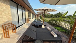 A modern outdoor lounge area with a pool, wooden deck, and outdoor seating. - Villa Rizière Ubud Center (Bali)