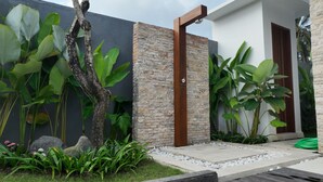 A modern building with a stone wall, a wooden door, and lush greenery. - Villa Rizière Ubud Center (Bali)