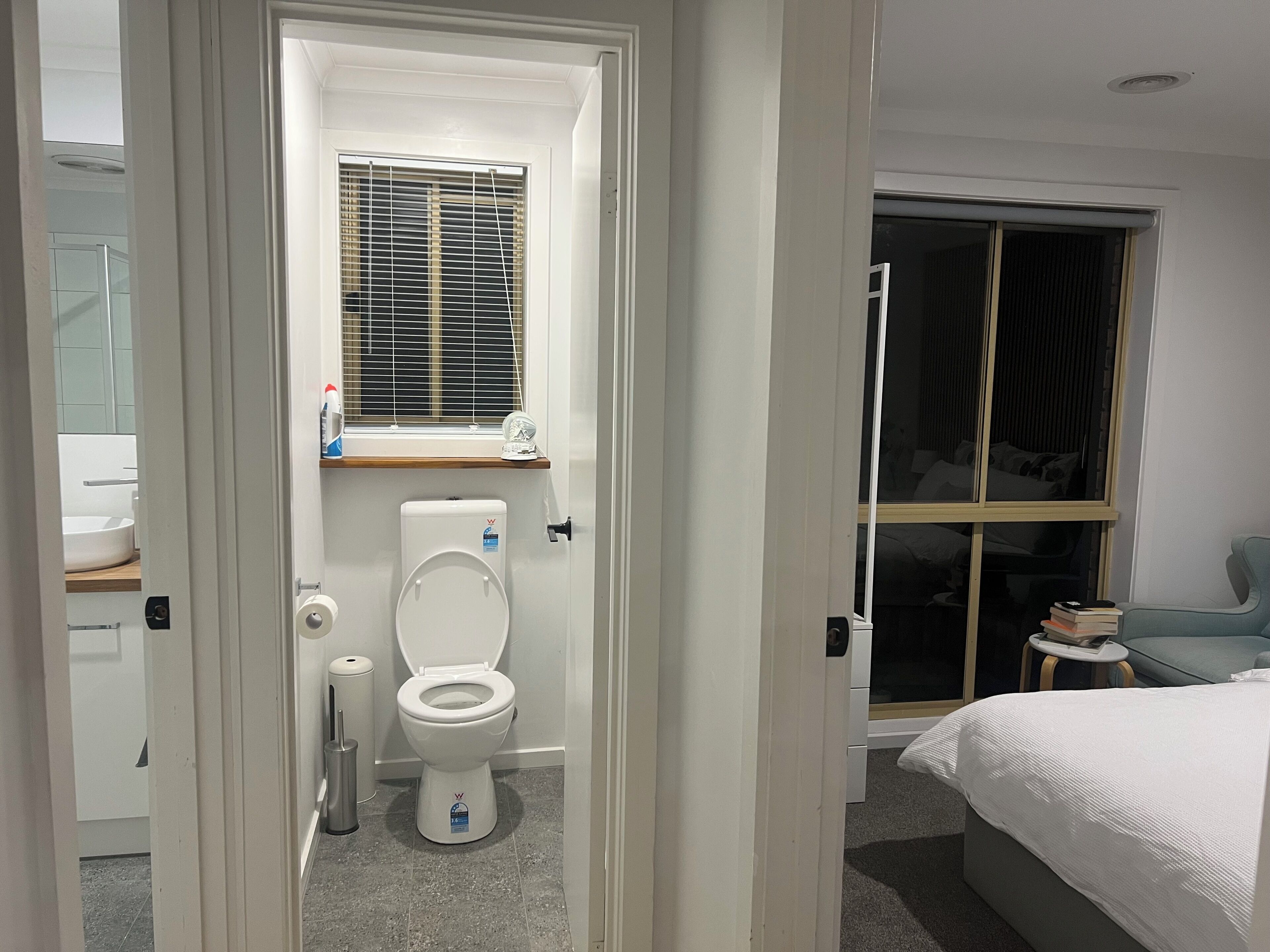 A modern bathroom with a toilet, bidet, and window with blinds.