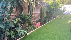 Un jardín bien cuidado con césped artificial, diversas plantas y una valla de madera.