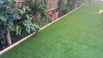 A well-maintained garden with artificial grass, various plants, and a wooden fence.