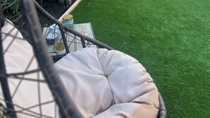 Un jardín con césped verde, cerca de madera y una hamaca.
