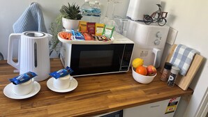 Una encimera de cocina con una tetera, microondas y diversos alimentos.