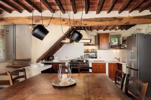 A rustic kitchen with exposed wooden beams, a wooden dining table with chairs, and a modern stainless steel refrigerator.
