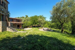 A stone building with a tiled roof, a stone staircase, and a garden with a bench.
