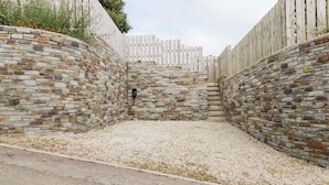 A stone-walled courtyard with a gravel ground, surrounded by a wooden fence. - Glendale (Port Isaac)