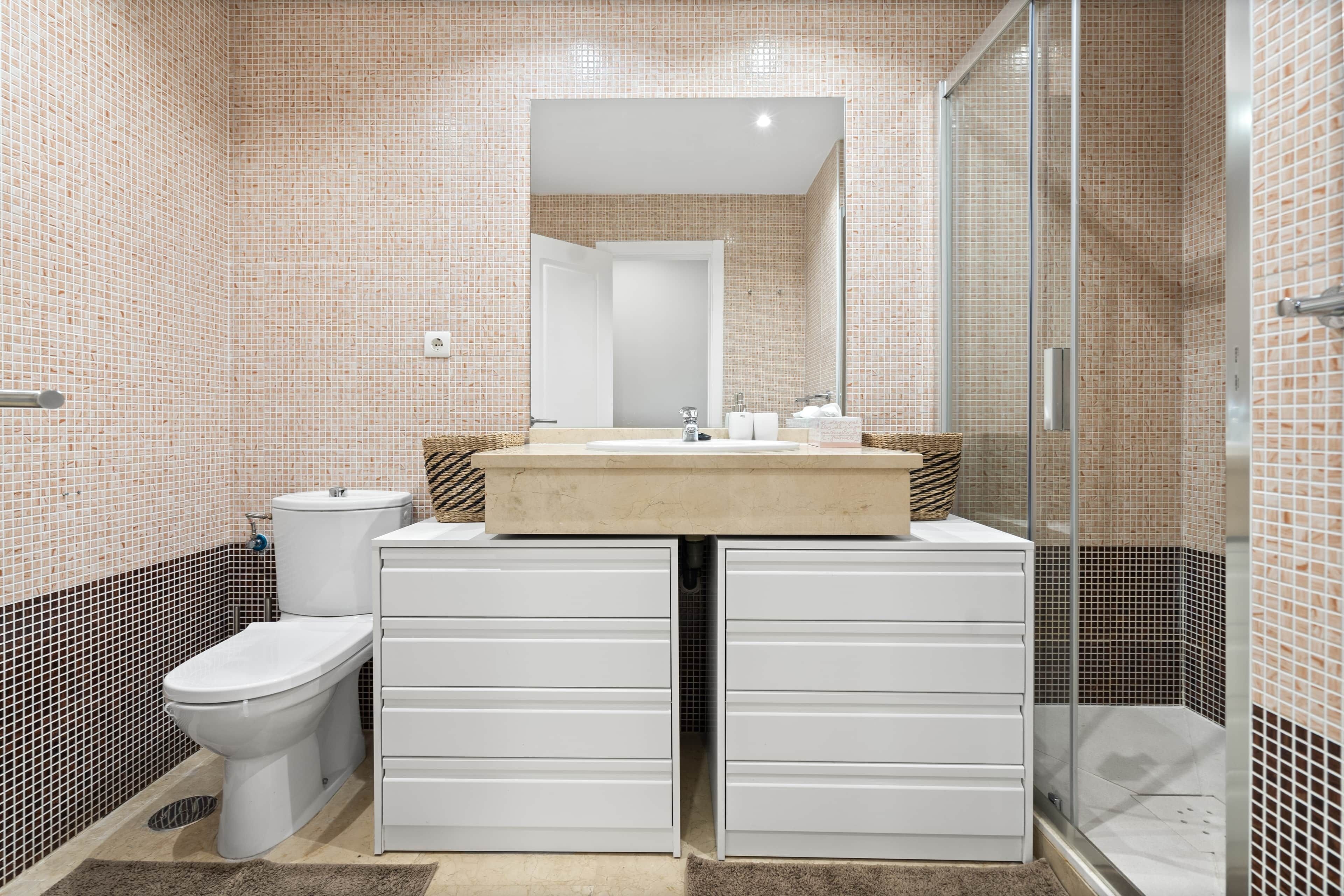 A bathroom with a tiled floor, a toilet, a sink with a mirror above it, and a shower area.