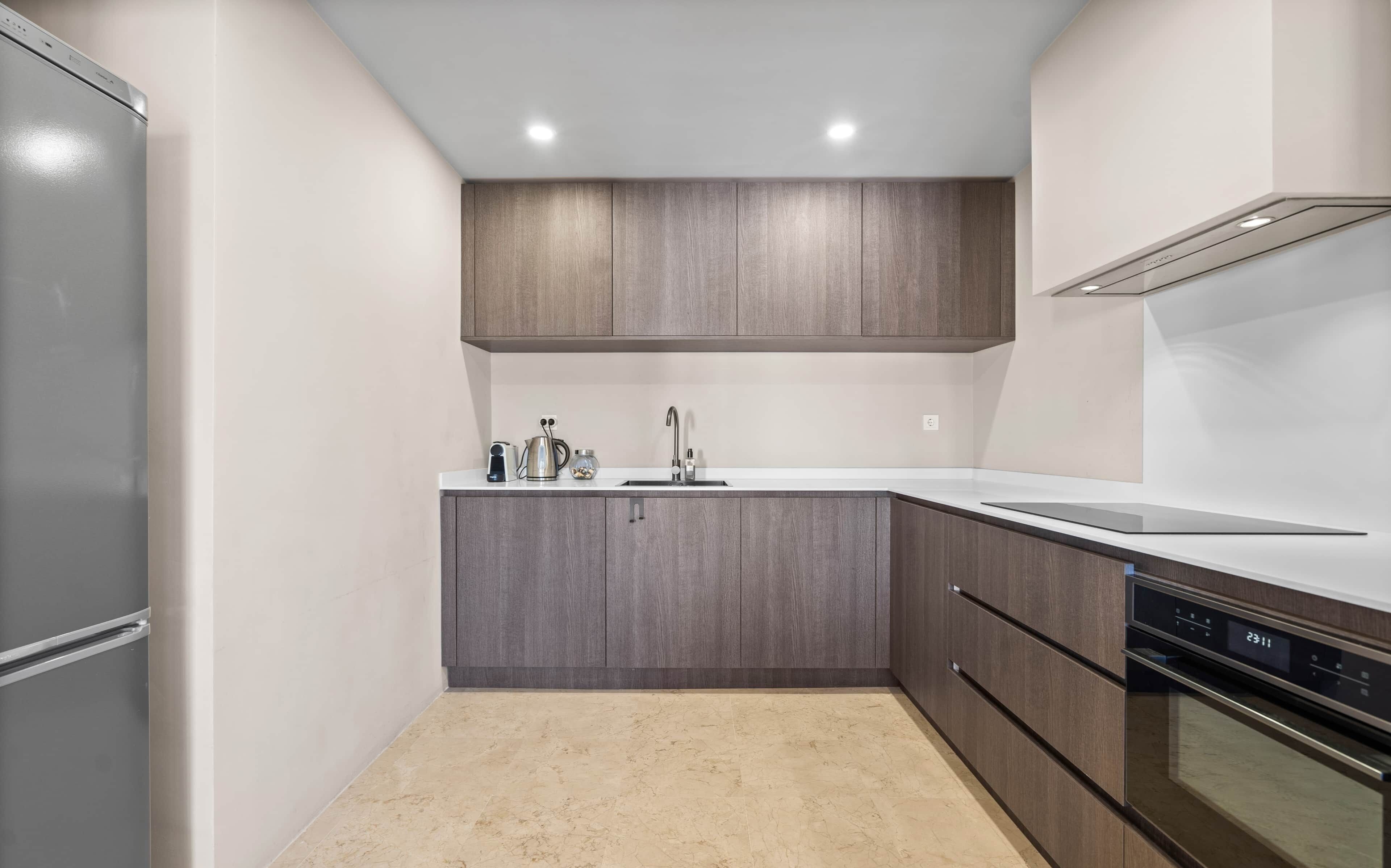 A modern kitchen with grey cabinets, a stainless steel refrigerator, a built-in oven, and a white countertop.