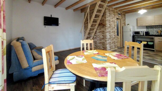 Una sala de estar acogedora con techo de madera, una mesa de comedor con sillas, un sofá, un televisor y una zona de cocina con microondas.