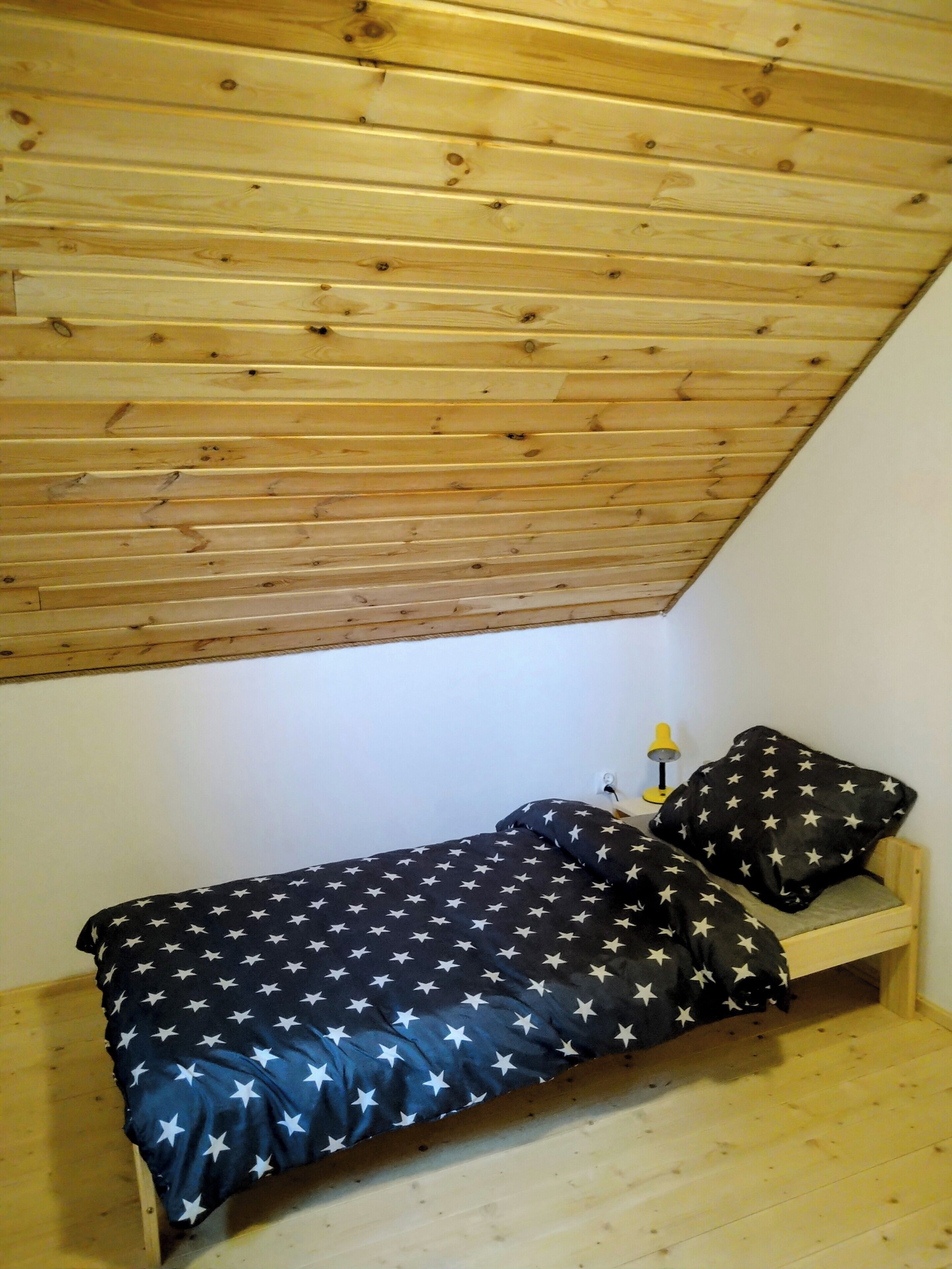 Una habitación pequeña con cama individual, techo inclinado y paredes de madera.