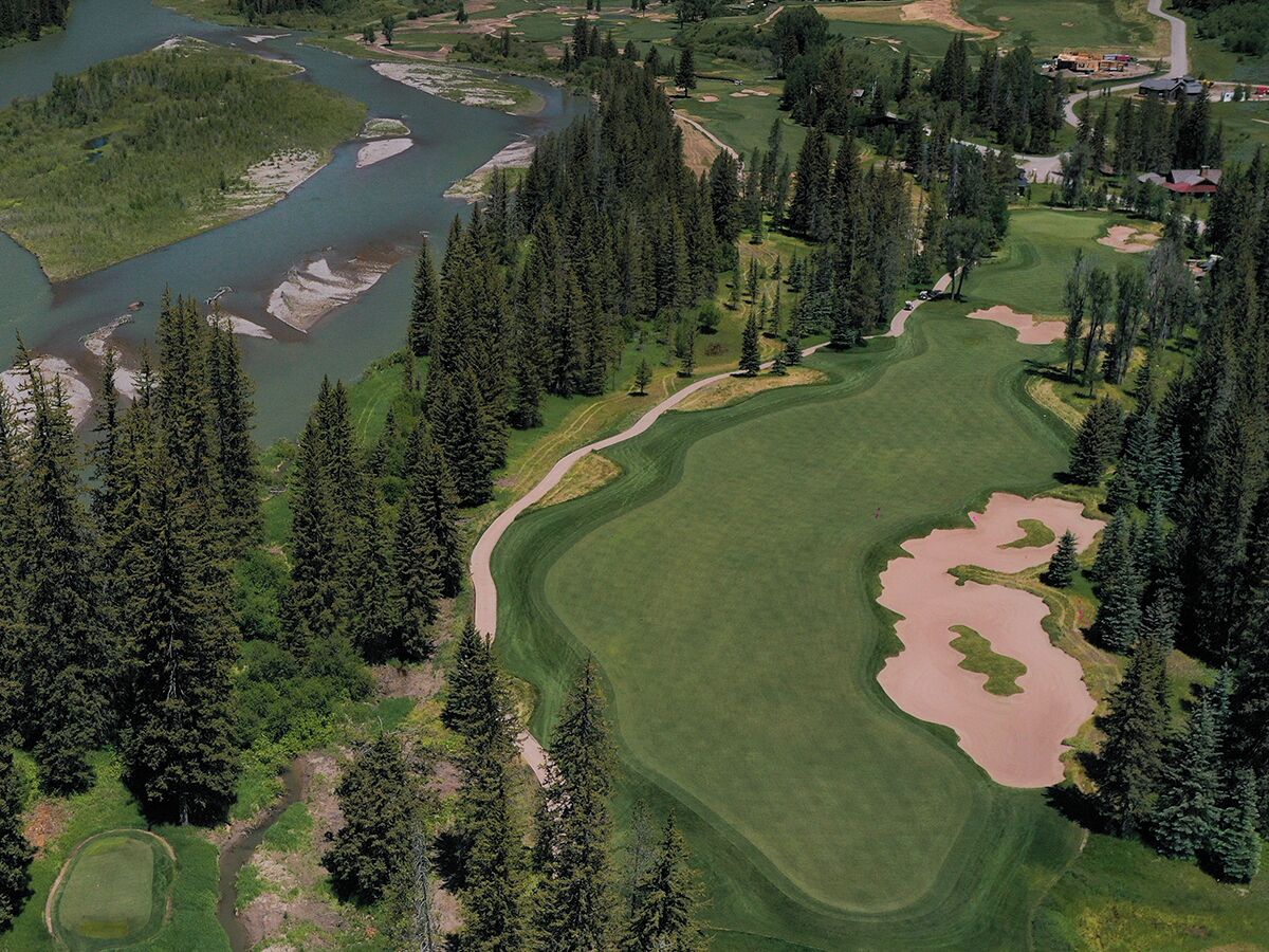 An aerial view of a golf course with a river, dense forest, and a large pond.