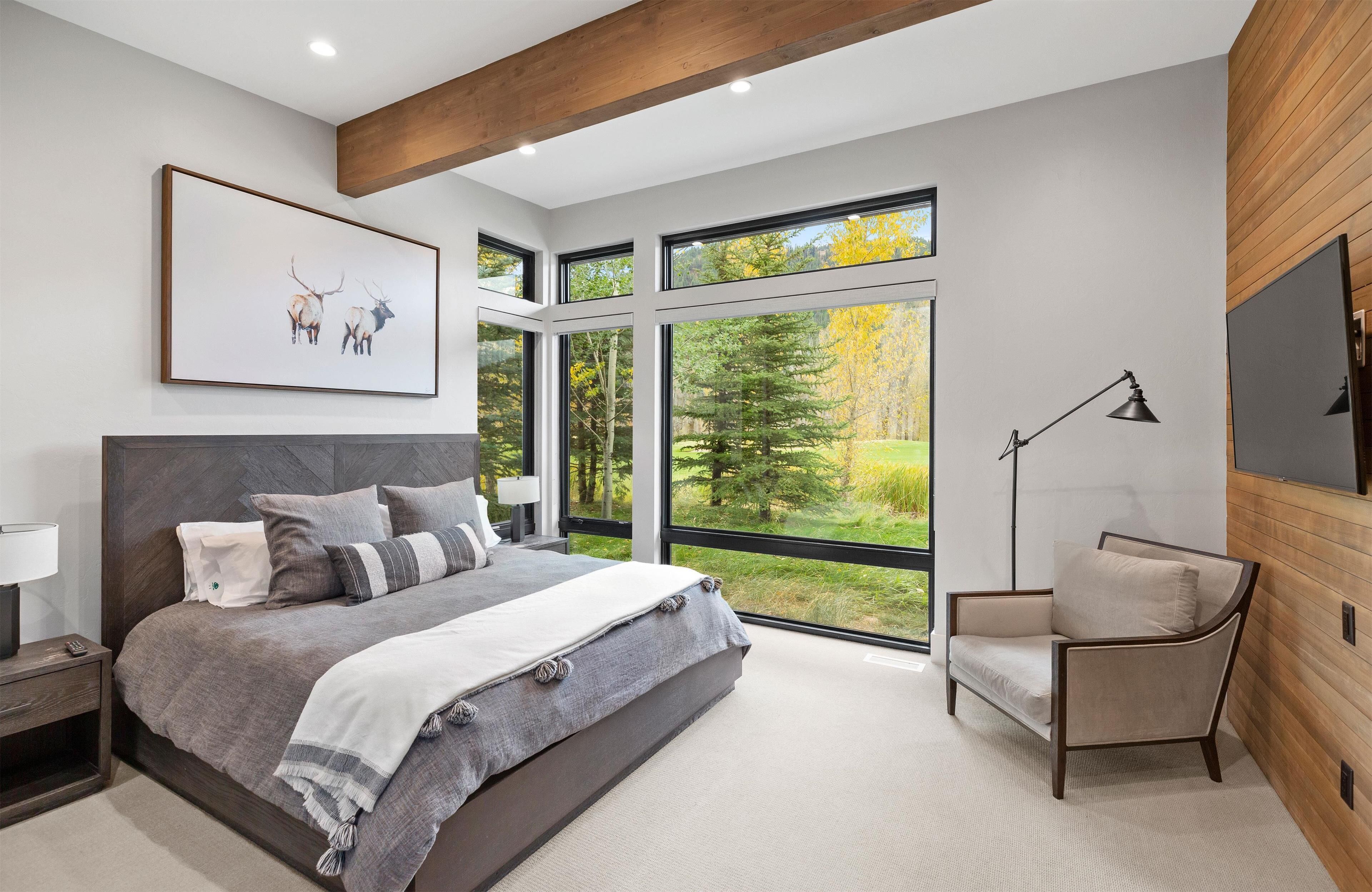 Een moderne slaapkamer met een groot bed, een stoel, een televisie en een raam met uitzicht op een bos.