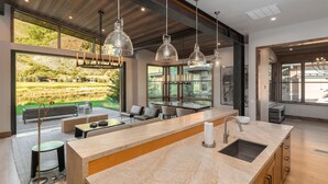 Une cuisine moderne dotée d’un grand îlot central, d’appareils électroménagers intégrés et de grandes fenêtres offrant une vue sur un paysage verdoyant.