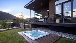 Une maison moderne dotée d’un jacuzzi, de grandes fenêtres et d’une terrasse.