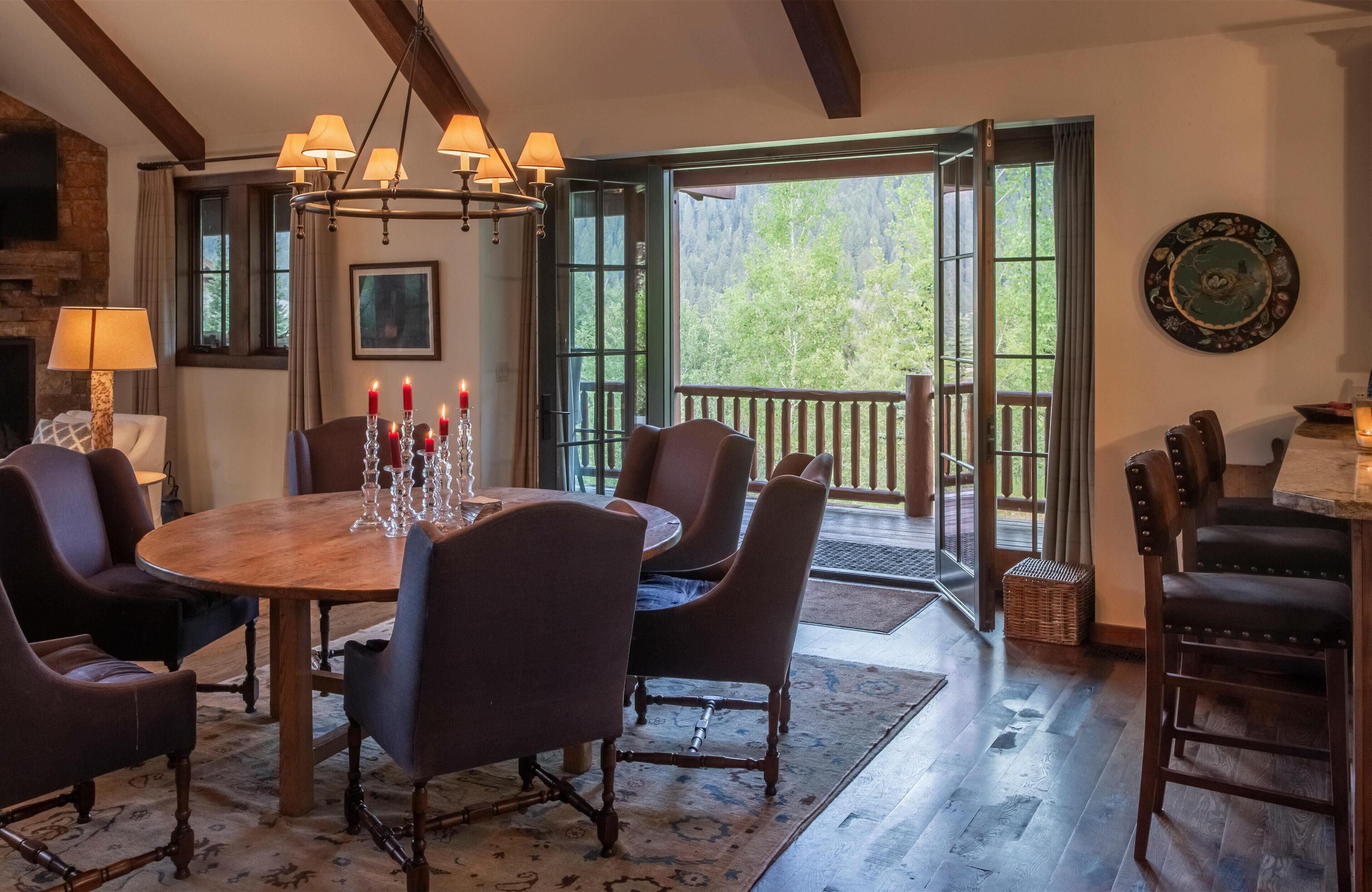 A dining area with a wooden table and chairs, candles, and a view of the outdoors.