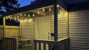 A wooden deck with a railing, a door, and string lights. - The Center Street Studio - Sleeps 4 (Searcy)