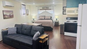 A compact room with a sofa, a bed, a kitchen area, and a small trash bin. - The Center Street Studio - Sleeps 4 (Searcy)